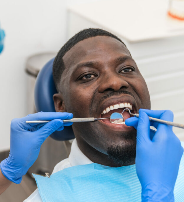 Dental hygienist examining an African male patient teeth using professional dental tools.